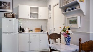 Una cocina con armarios blancos, cafetera, hervidor y tabla de cortar de madera.