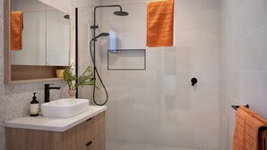 A modern bathroom with a white sink, a mirror, a shower with a handheld showerhead, and a towel rack. - Cosy Edge Studio-Modern stuido, quiet and walking distance to Farmers Arms Hotel (Daylesford)