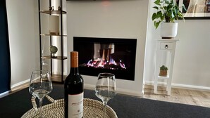 A cozy living room with a fireplace, a wine bottle, and two glasses on a woven mat. - Cosy Edge Studio-Modern stuido, quiet and walking distance to Farmers Arms Hotel (Daylesford)