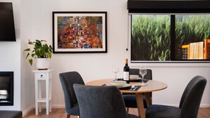 A dining area with a round table, four grey chairs, a potted plant, a framed artwork, and a window with a view of greenery and a building. - Cosy Edge Studio-Modern stuido, quiet and walking distance to Farmers Arms Hotel (Daylesford)