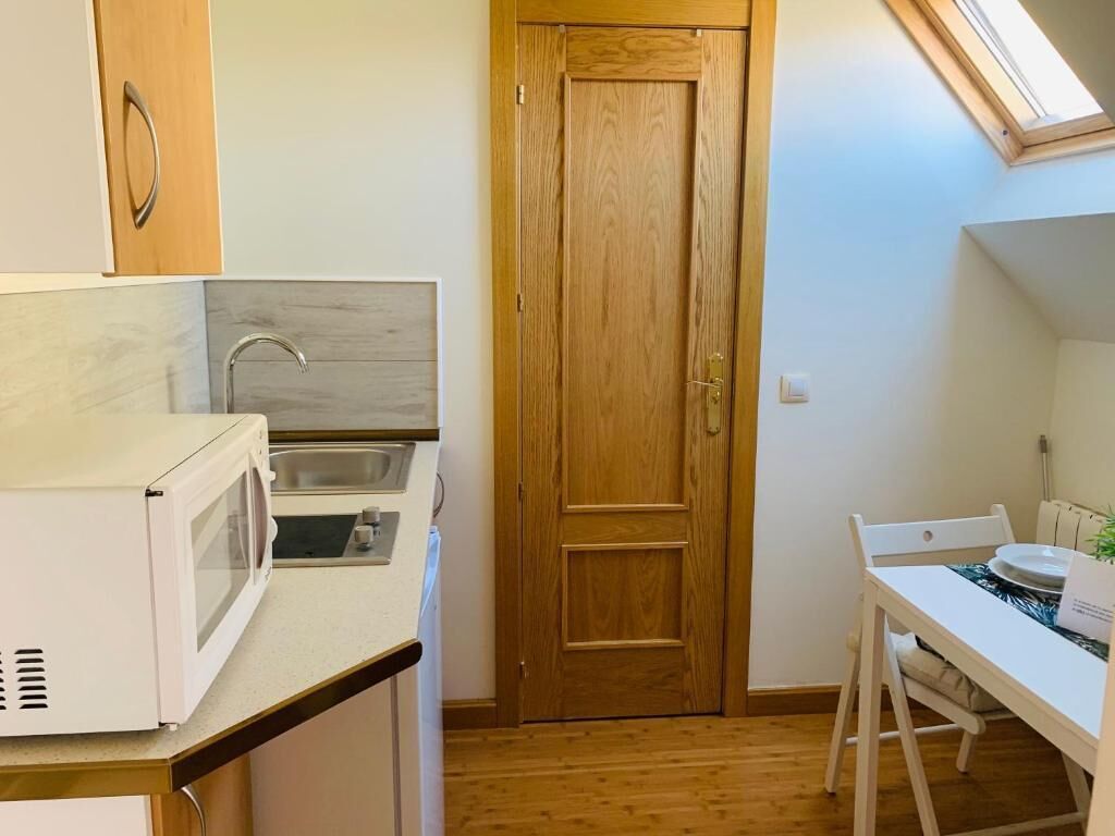 A compact kitchen with a microwave, sink, and wooden door.