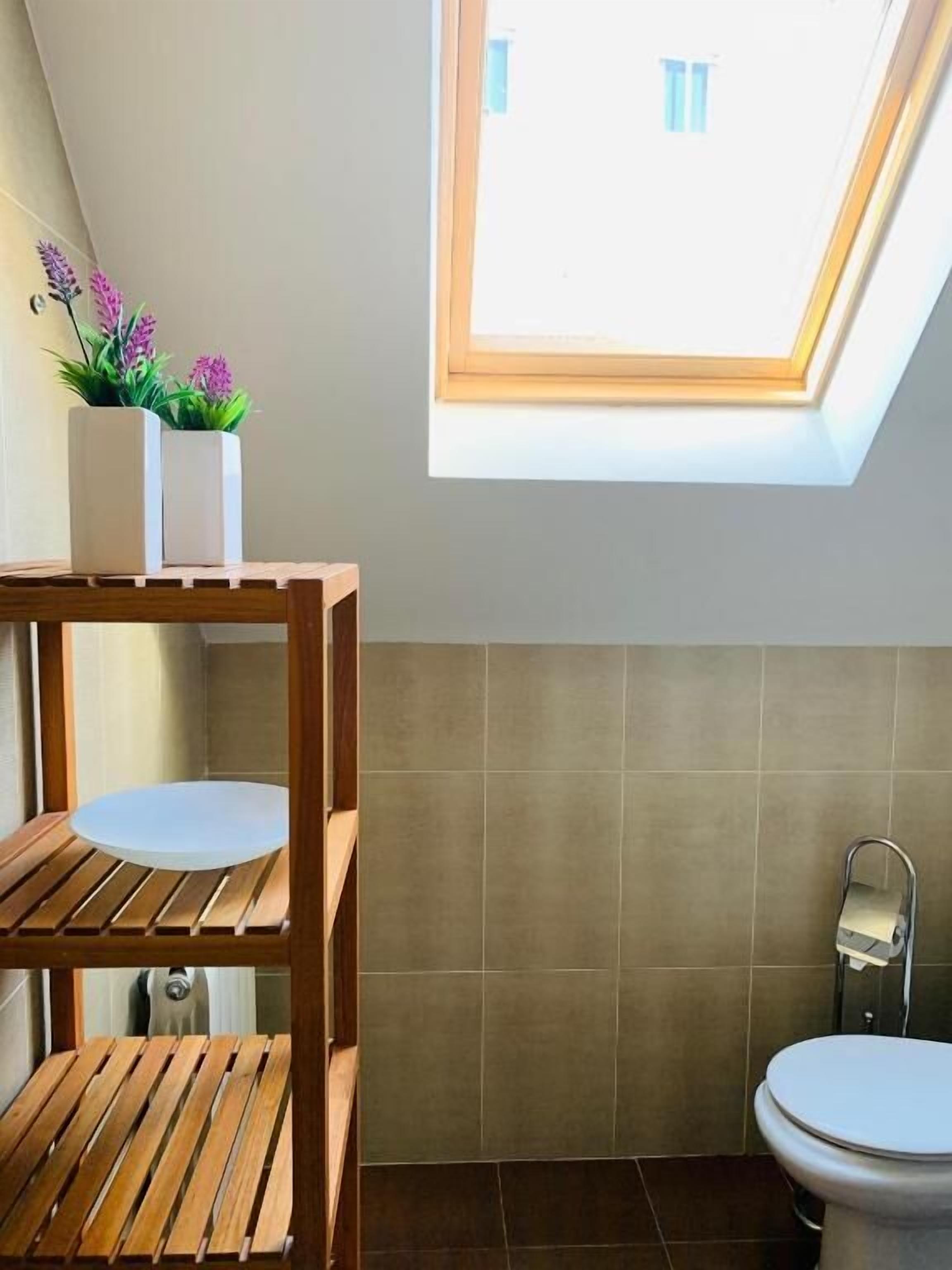 A modern bathroom with a skylight, a wooden shelf unit, and a toilet.