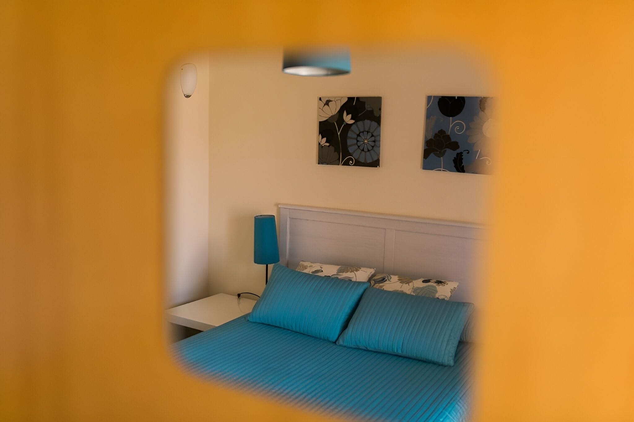 Un dormitorio con cama, mesita de noche, lámpara y dos obras de arte en la pared.