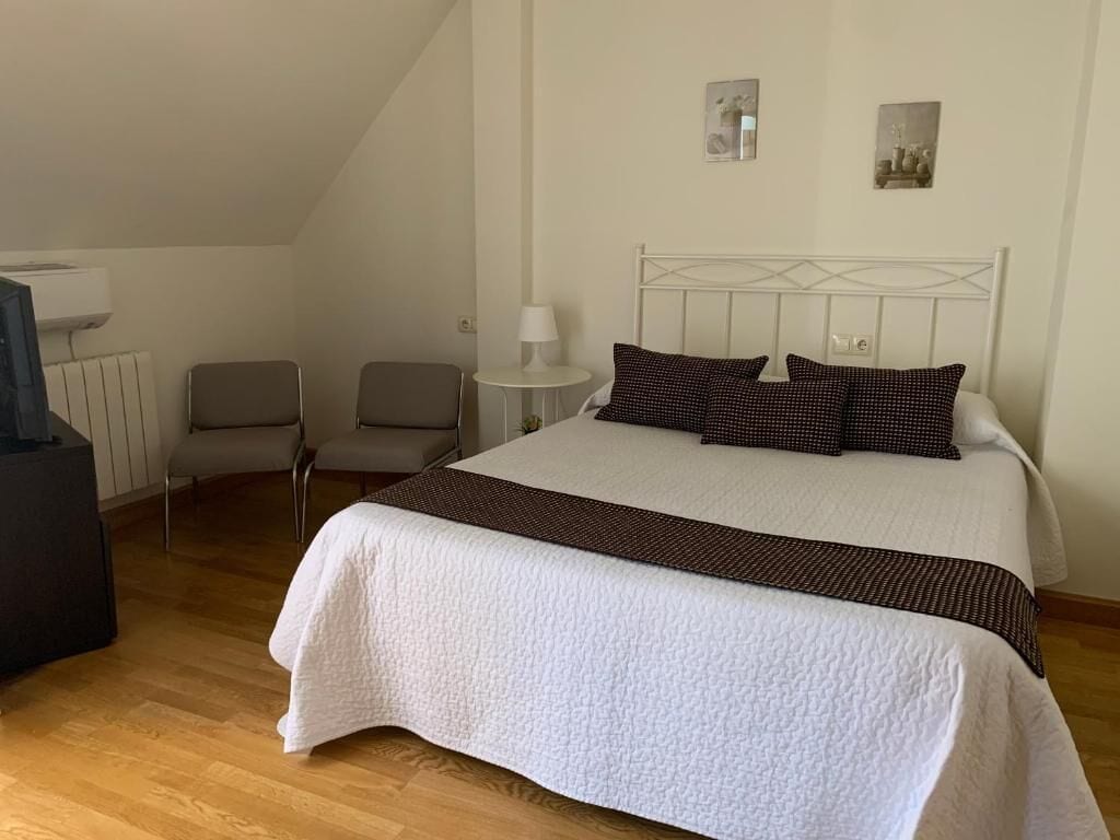 Una camera da letto con un letto, due sedie, un tavolino e una lampada, e un termosifone.