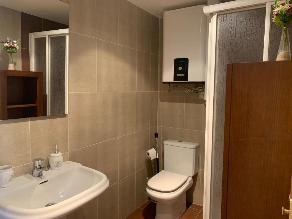 A bathroom with a white sink, toilet, and a small shelf with a device.