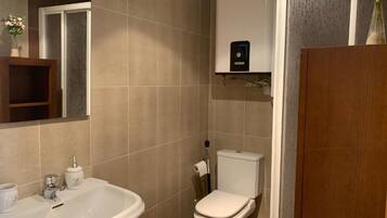 A bathroom with a white sink, toilet, and a small shelf with a device.