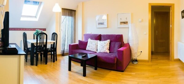 A living room with a purple sofa, a coffee table, and a dining area with chairs and a table. - Aticos La Aliseda by Valdesierra (Bejar)