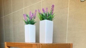 Puinen hylly, jonka päällä on kaksi valkoista kukkaruukkua ja alimmalla hyllyllä valkoinen alusta.