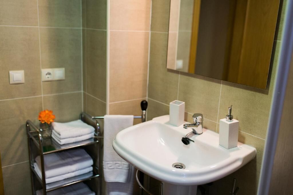 Un baño con un lavamanos blanco, un espejo, un perchero con toallas dobladas y una pequeña flor naranja.