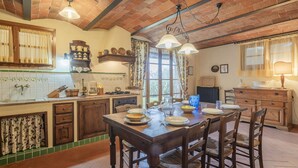 A rustic kitchen with wooden cabinets, a dining table set for four, and a large window with curtains. - Casa Viola Pool, Wifi, Montaione (Montaione)