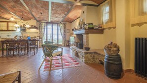 A spacious living area with a stone fireplace, a dining table with chairs, and a large window with curtains. - Casa Viola Pool, Wifi, Montaione (Montaione)