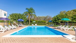 A rectangular swimming pool with clear blue water, surrounded by white lounge chairs and umbrellas.