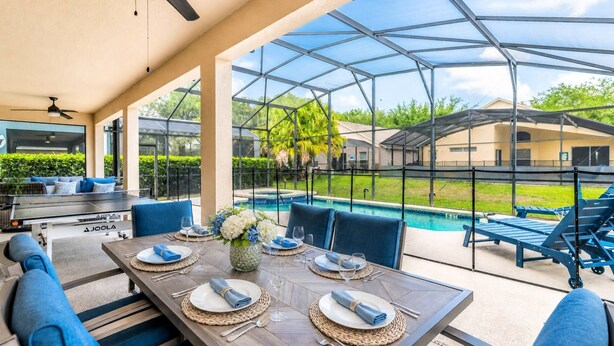 A covered outdoor dining area with a pool view, a grill, and blue seating. - Ultimate Family Retreat with Themed Rooms, Private pool and spa, theater & games! Pet Friendly (Kissimmee)