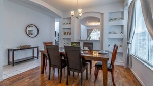 A dining area with a wooden table and chairs, a chandelier, and built-in shelving with decorative items. - Ultimate Family Retreat with Themed Rooms, Private pool and spa, theater & games! Pet Friendly (Kissimmee)