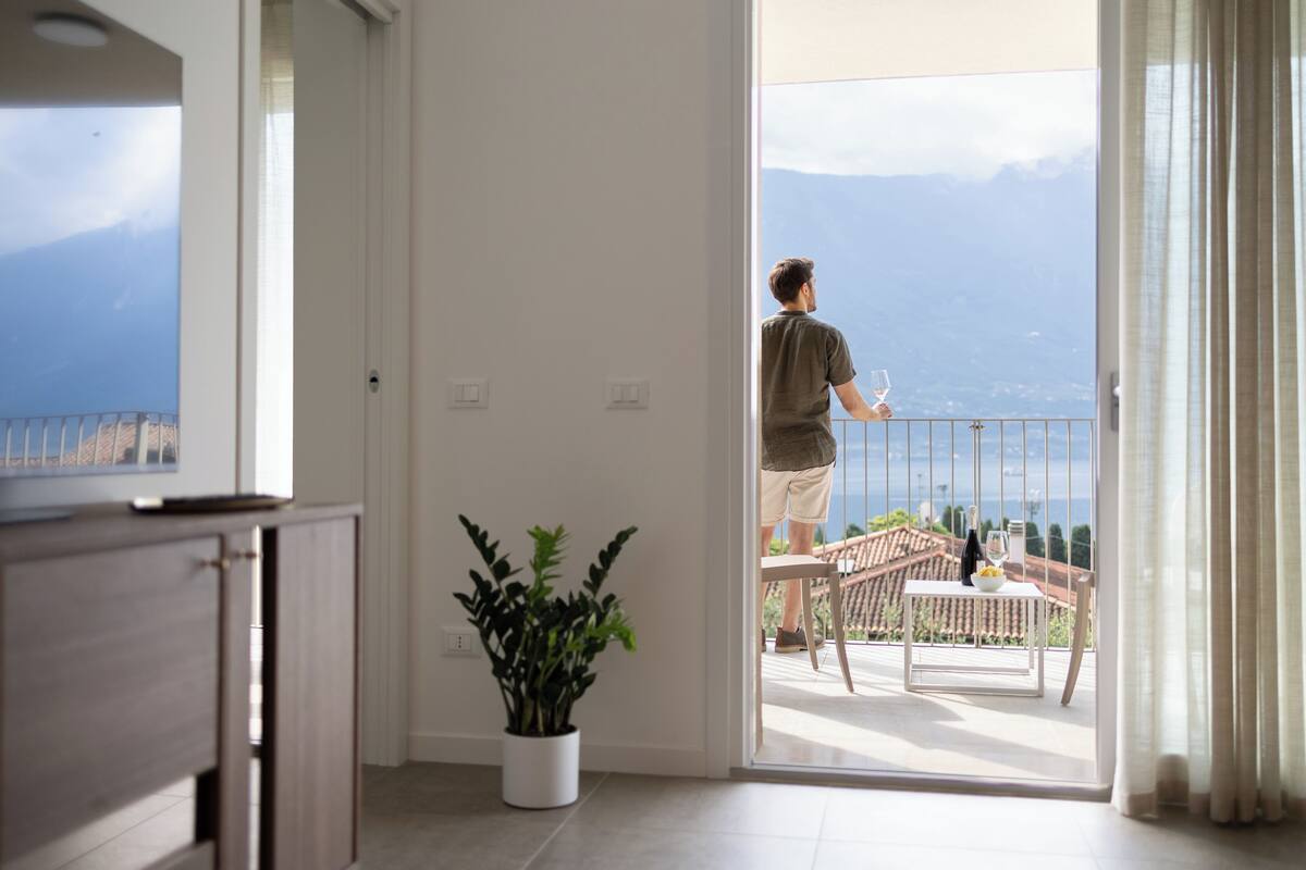 Una stanza con balcone, una pianta in vaso e vista mare e montagne.