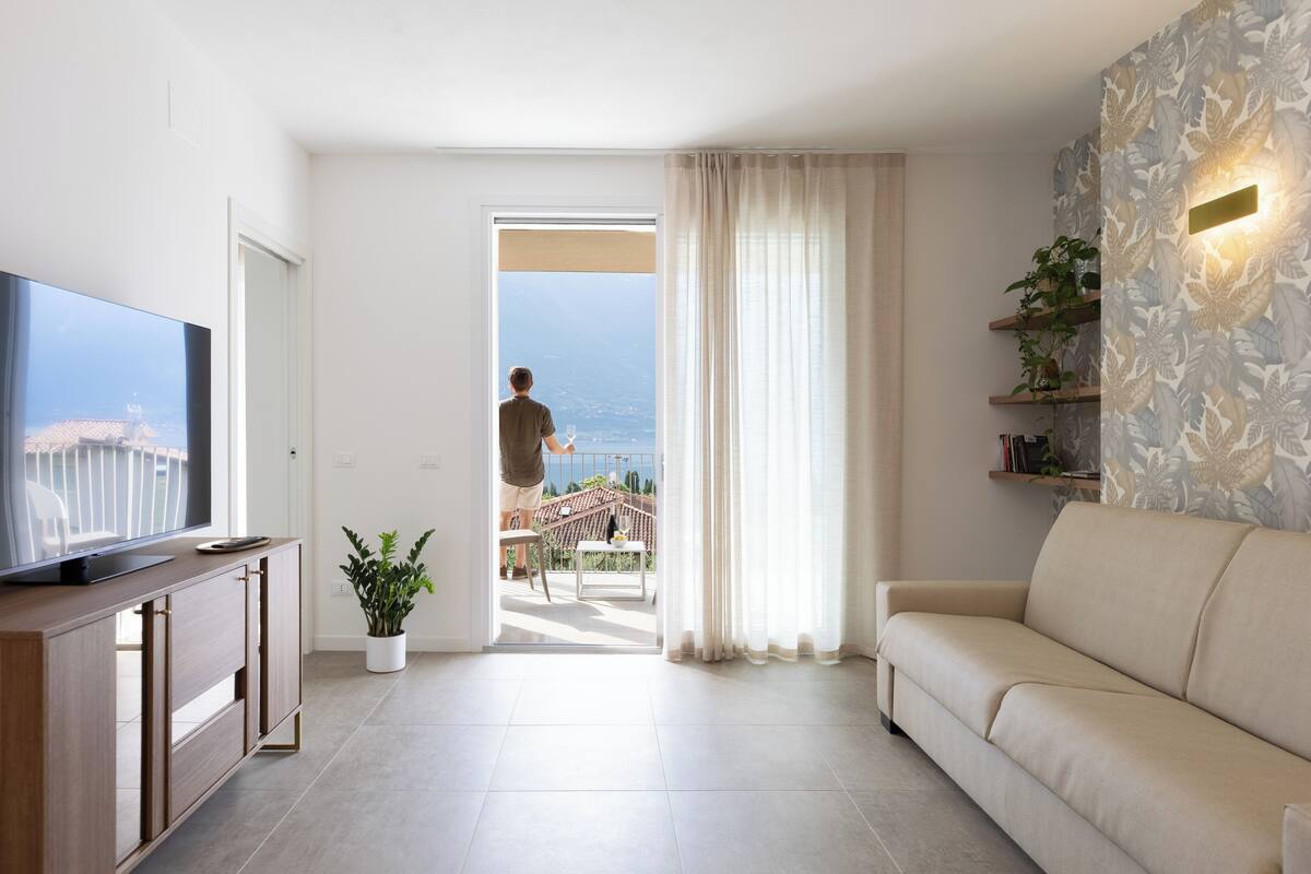 Un soggiorno moderno con una televisione a schermo piatto, un divano, una pianta in vaso e un balcone vista mare.