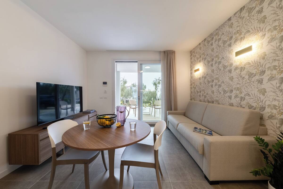 Un soggiorno moderno con un divano, un tavolo da pranzo con sedie, una televisione a schermo piatto e un balcone con porte scorrevoli.
