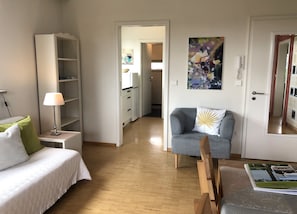 A room with a bed, a chair, a desk, a bookshelf, and a door leading to another room.