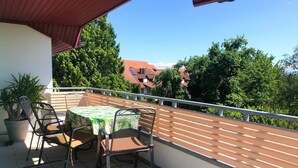 A balcony with a table and chairs, a potted plant, and a view of houses and trees. - Apartment "Panorama" with Lake and Mountain Views, Wi-Fi (Friedrichshafen)