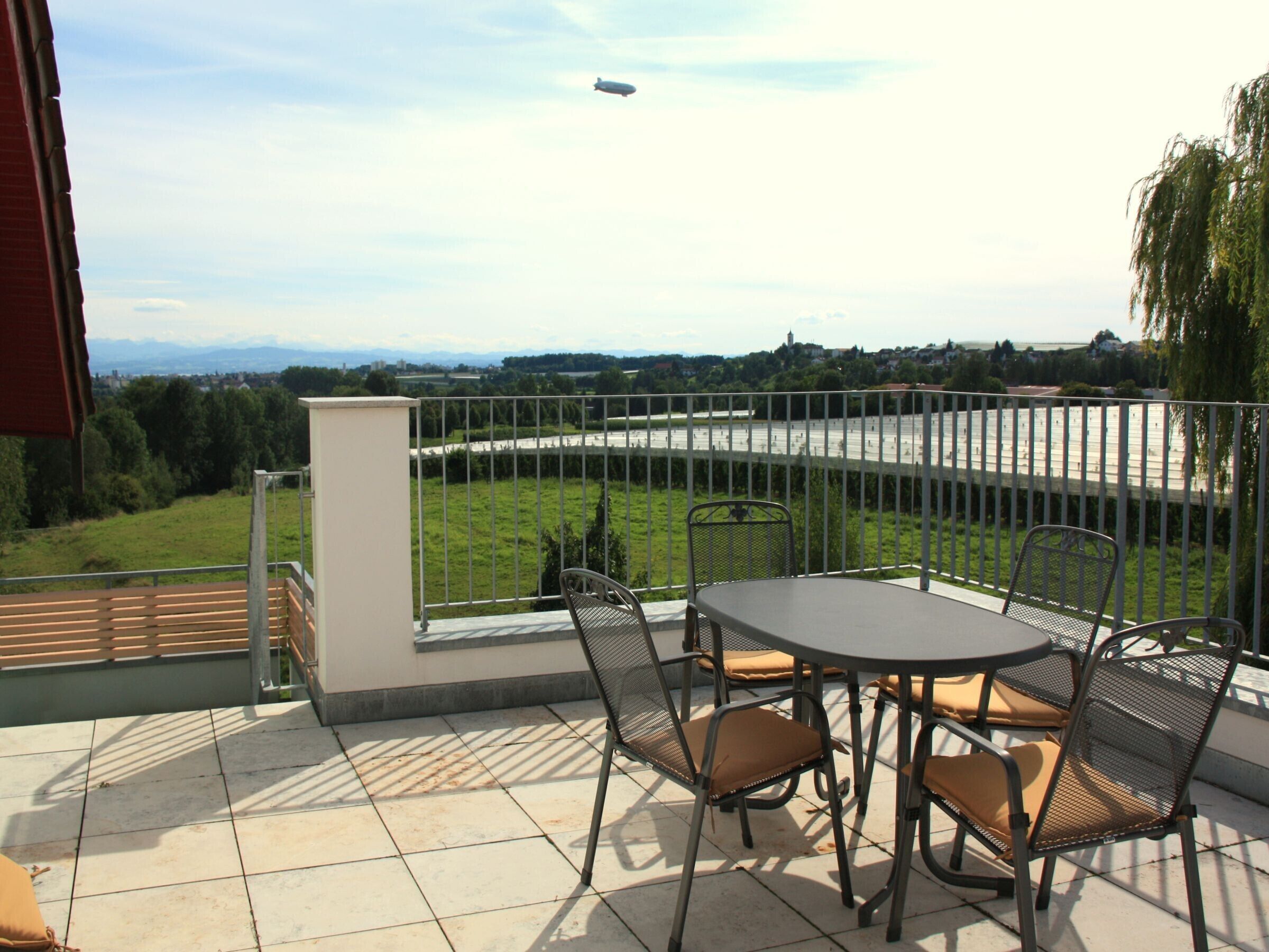 Eine Terrasse mit Tisch und Stühlen, Blick auf einen Fluss und eine weite Landschaft.