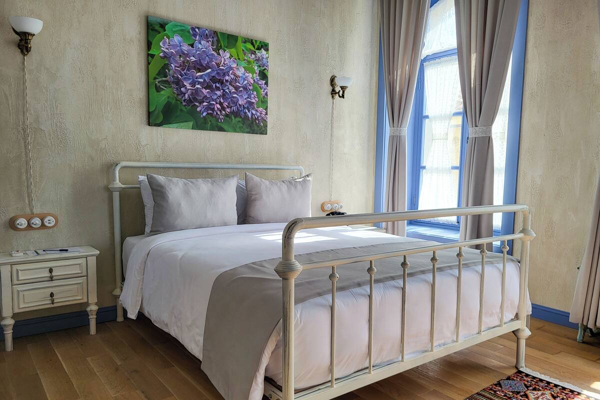 Un dormitorio con estructura de cama de metal blanco, una mesita de noche con lámpara y un cuadro de flores colgado en la pared.