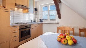 A kitchen with wooden cabinets, a stove, and a table with apples. - Haus Hilebrand - Apartment '4, 75 sqm' with Shared Garden, Balcony and Wi-Fi (Kressbronn a. B.)