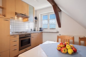 A kitchen with wooden cabinets, a stove, and a table with apples. - Haus Hilebrand - Apartment '4, 75 sqm' with Shared Garden, Balcony and Wi-Fi (Kressbronn a. B.)