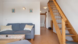 A living room with a sofa, a coffee table, and a wooden staircase. - Haus Hilebrand - Apartment '4, 75 sqm' with Shared Garden, Balcony and Wi-Fi (Kressbronn a. B.)