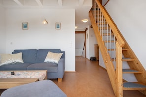 A living room with a sofa, a coffee table, and a wooden staircase. - Haus Hilebrand - Apartment '4, 75 sqm' with Shared Garden, Balcony and Wi-Fi (Kressbronn a. B.)