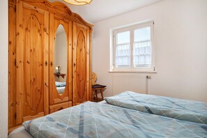 Une chambre avec une armoire en bois, une fenêtre donnant sur un beau paysage et un lit recouvert d’une couvre-lit à motifs.