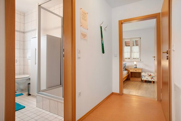 A hallway with a bathroom, a bed, a nightstand, and a mirror. - Haus Hilebrand - Apartment '5, 45 sqm' with Shared Garden, Balcony and Wi-Fi (Kressbronn a. B.)