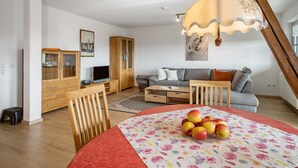 A modern living room with a sofa, a dining table with apples, a wooden cabinet, and a television.