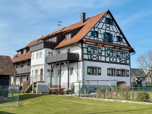 Une maison traditionnelle à colombages, dotée d’un toit en pente, d’un balcon et d’une cour clôturée.