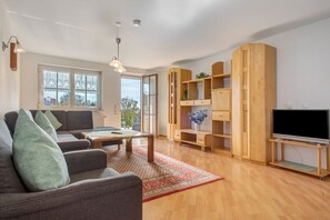 Uma sala de estar moderna com um sofá, mesa de centro, estantes de madeira e uma televisão.