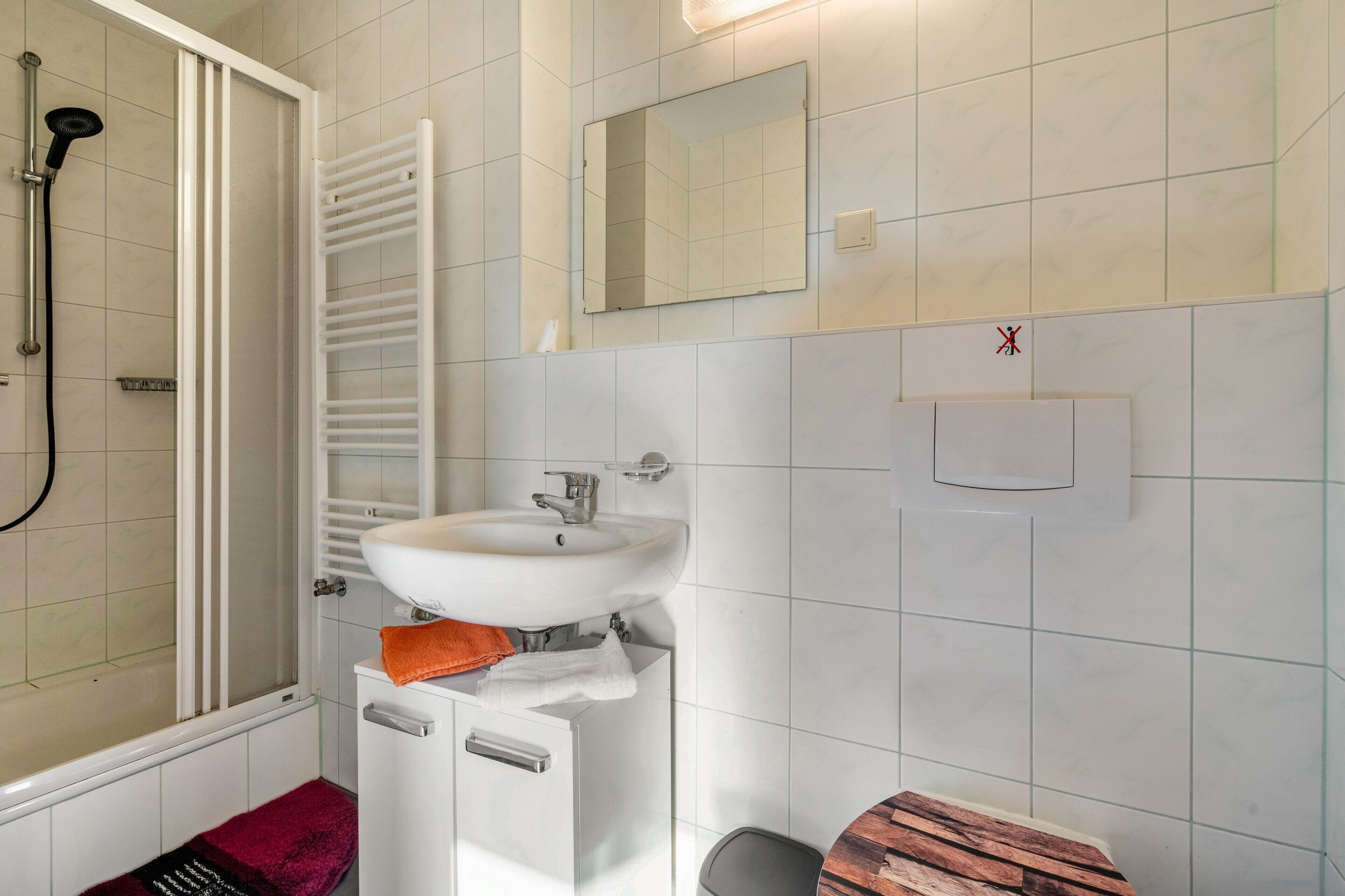 Un bagno con doccia, lavandino, specchio e porta asciugamani.
