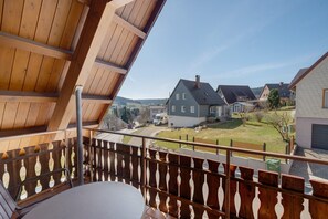 Een balkon met houten leuning, een tafel en uitzicht op huizen en een weg.