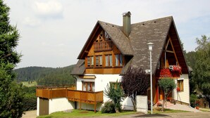 A traditional wooden house with a sloped roof, a balcony, and a small attached shed.