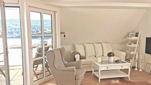 Una sala de estar moderna con sofá, sillón, mesa de centro y puerta de cristal que da a un área exterior.