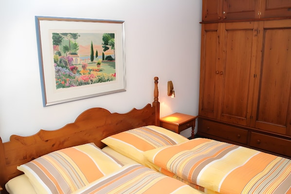 A bedroom with a wooden headboard, a bed with striped bedding, a framed painting, a nightstand with a lamp, and a wooden wardrobe.