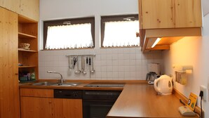 Una cocina con armarios de madera, lavavajillas, hervidor y ventana con cortinas.