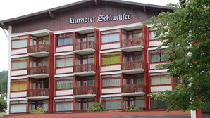 Un hotel de varios pisos con balcones, un letrero que dice 'Kurhotel Schluchtsee' y vistas de la vegetación circundante.