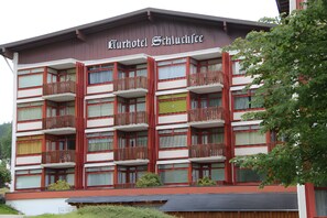 Monikerroksinen hotelli, jossa on parvekkeet, kyltti, jossa lukee ”Kurhotel Schluchtsee”, ja näkymä ympäröivään vehreään maisemaan.