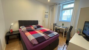 Une chambre à coucher avec un lit, un bureau, une chaise, une télévision et une fenêtre.