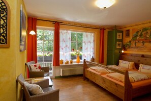 A room with a bed, two chairs, a window with curtains, a radiator, and a wall with a mural.
