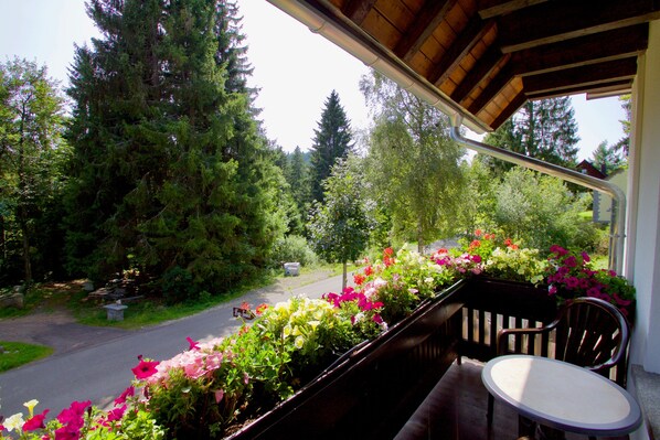 A balcony with a view of a road and forest, a chair, and a table.