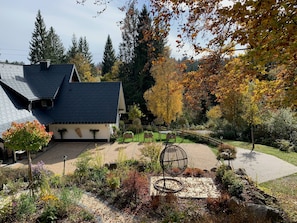 Une maison avec un toit en pente, un jardin où poussent différentes espèces de plantes et une sculpture sphérique en métal.