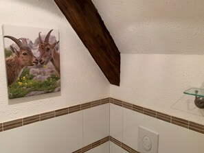 Een badkamer met witte wanden, een balk van donker hout, een glazen plank en een afbeelding van twee geiten.