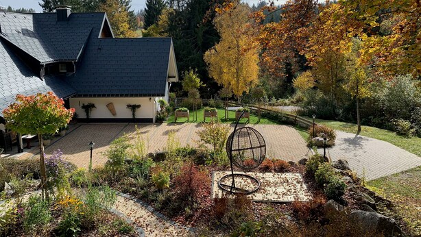 A house with a sloped roof, a garden with various plants, and a spherical metal sculpture.
