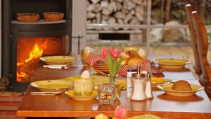 Ein Esstisch gedeckt mit Tellern, einer Karaffe, einer Tasse, einer Blumenvase, Salz- und Pfefferstreuern sowie einem Brotkorb.