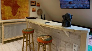 Ein Zimmer mit einer großen Karte Afrikas, einer Bar mit Hockern, einem Fernseher, der eine Landschaft zeigt, und Wandbildern.